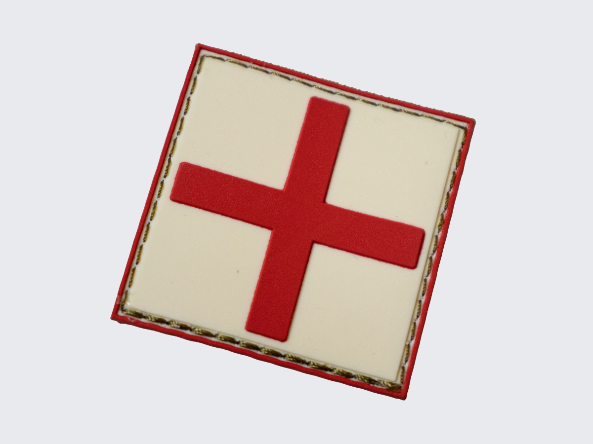 Valkoinen PVC hihamerkki punaisella ristillä. Tarranauhakiinnitys. White PVC patch with a red cross. Velcro patch.