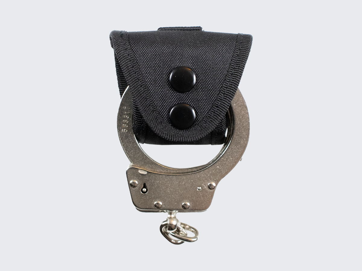 Pienikokoinen ja erittäin kevyt käsirautapidike vartijan tai järjestyksenvalvojan varustevyölle. A compact and extremely lightweight handcuff holder for a guard or security personnel equipment belt.